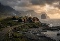 Isolated village of wooden houses on a coastal cliff surrounded by mountains at sunset